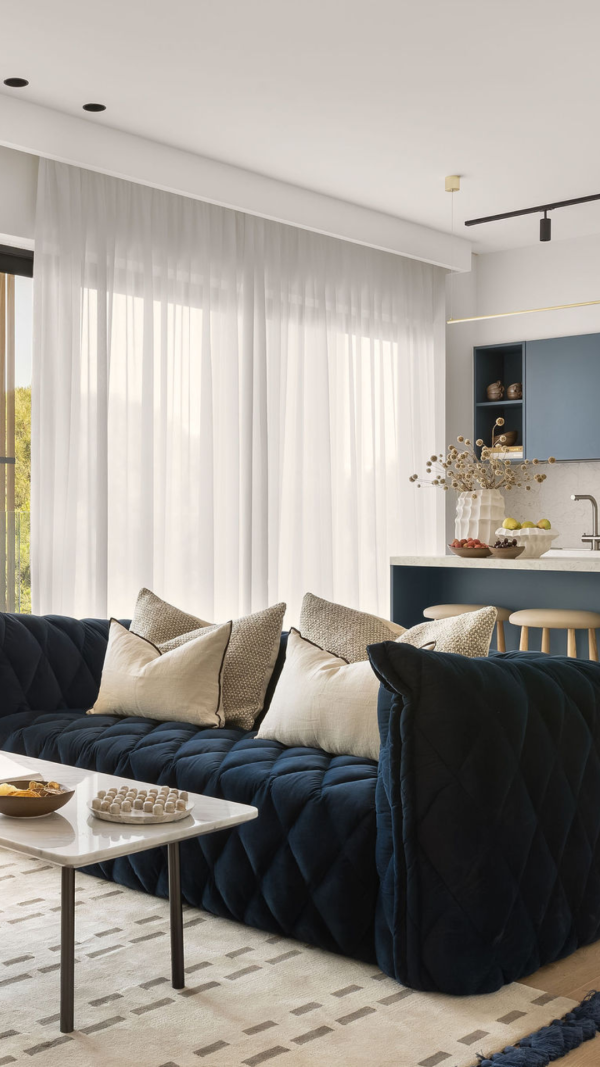 Elegant apartment living space at White City Limassol Aparthotel, featuring a deep blue velvet sofa, modern kitchenette, and sheer curtains with soft natural lighting.