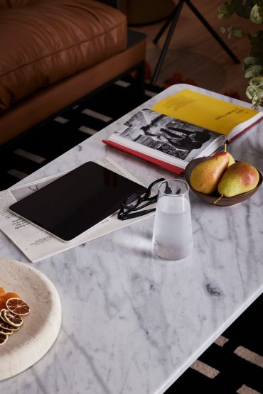 Marble coffee table with an open book, tablet, glasses, a glass of water, and a bowl of pears at White City Limassol Hotel.